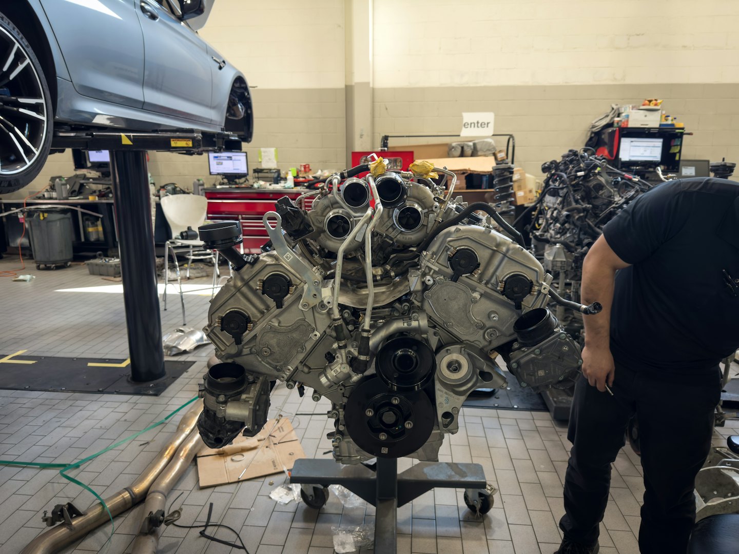 Mechanic observing a V-style car engine on a stand in a shop.